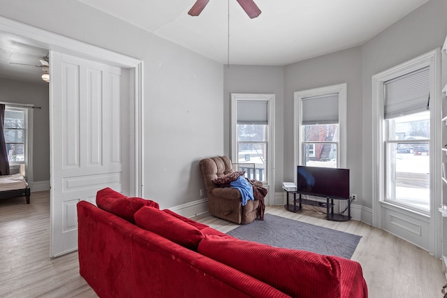 living area featuring light wood-type flooring, plenty of natural light, baseboards, and ceiling fan