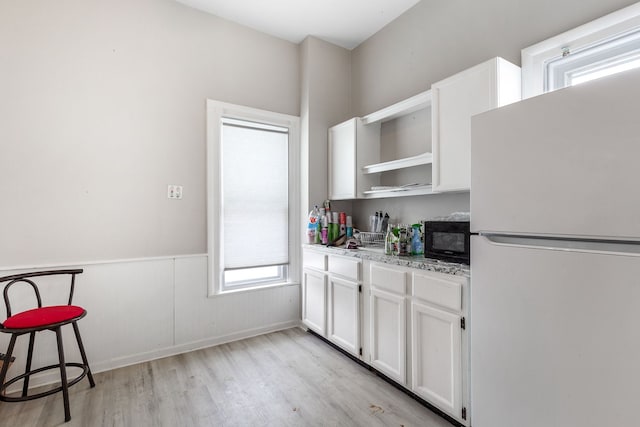 kitchen featuring freestanding refrigerator, white cabinets, wainscoting, light stone countertops, and black microwave