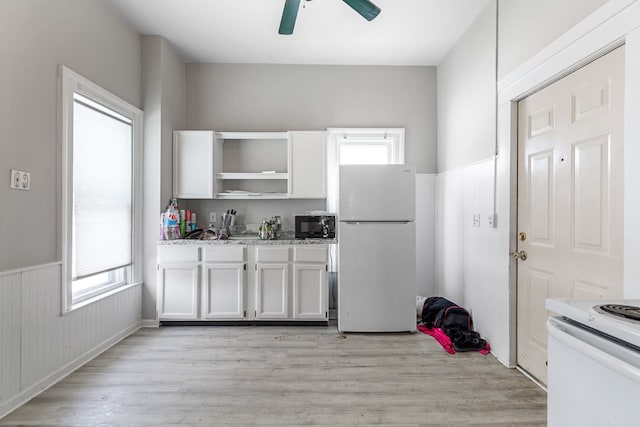 kitchen with white appliances, a ceiling fan, white cabinets, wainscoting, and light wood finished floors