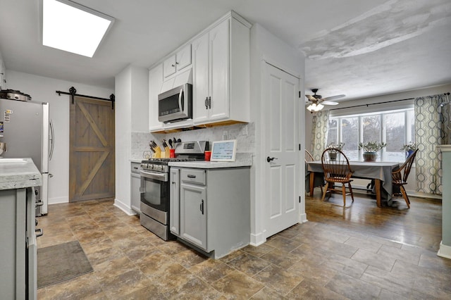 kitchen featuring stainless steel appliances, gray cabinets, light countertops, decorative backsplash, and a barn door