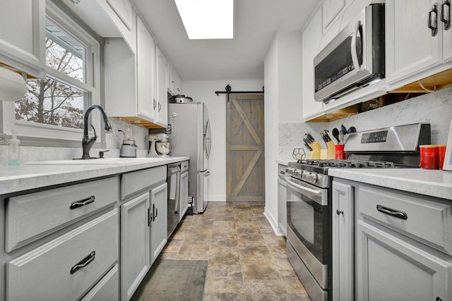 kitchen featuring stainless steel appliances, light countertops, decorative backsplash, a barn door, and a sink