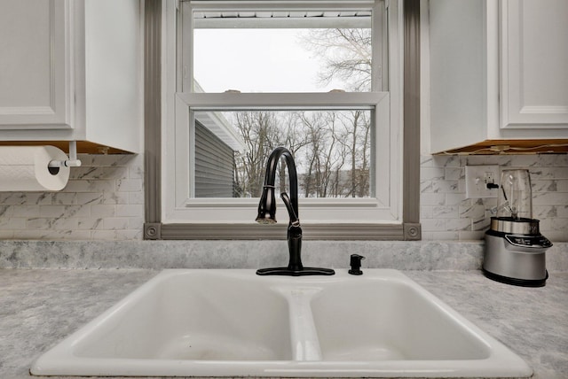 interior details featuring backsplash, a sink, and white cabinetry