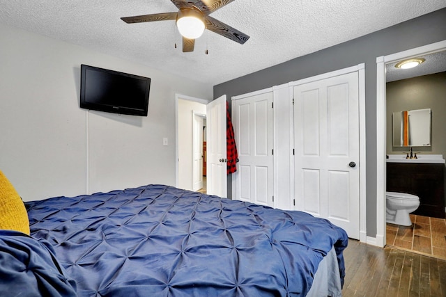 bedroom featuring multiple closets, a sink, a textured ceiling, and dark wood-style flooring