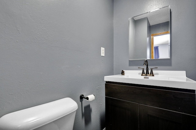 half bath featuring a textured wall, vanity, and toilet