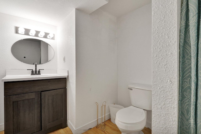 full bath with toilet, baseboards, wood finished floors, and vanity