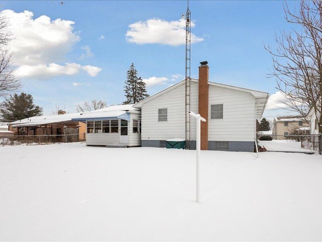 snow covered house featuring a chimney and fence