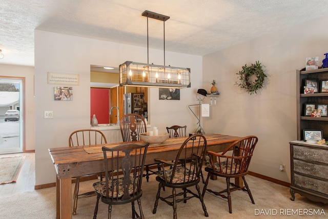 dining room with light carpet, a textured ceiling, and baseboards