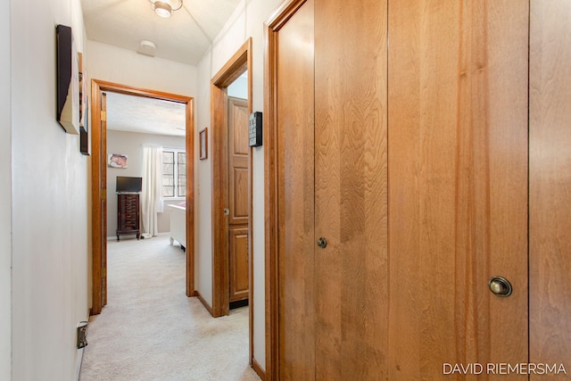 corridor featuring light colored carpet and baseboards