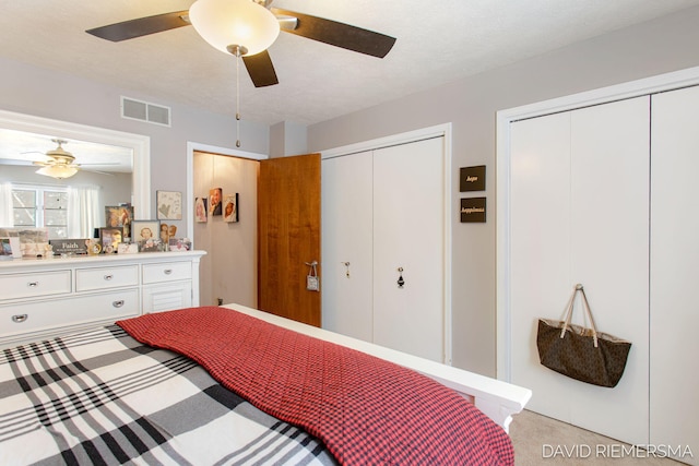 bedroom featuring visible vents, ceiling fan, light carpet, and two closets