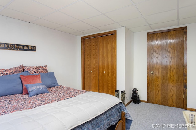 carpeted bedroom featuring a drop ceiling and baseboards