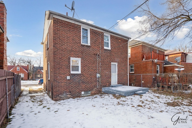 snow covered back of property featuring a residential view, brick siding, and fence