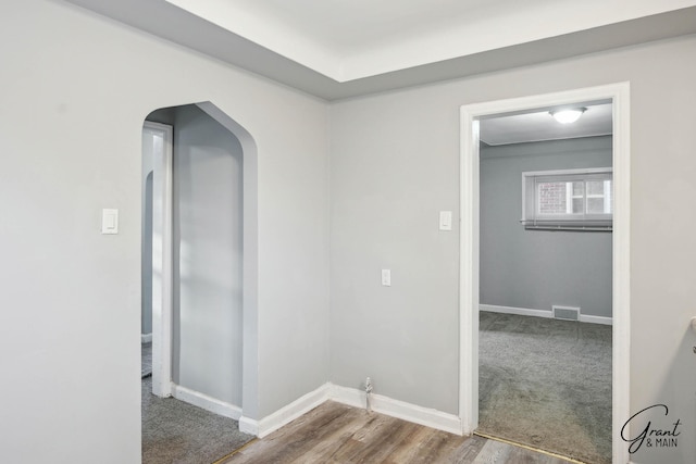 hall featuring arched walkways, wood finished floors, visible vents, and baseboards