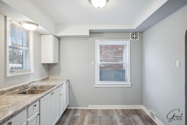 kitchen featuring wood finished floors, a sink, white cabinetry, baseboards, and light countertops