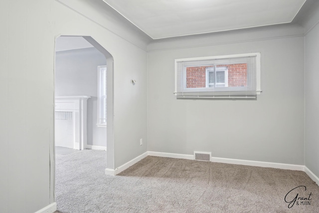 carpeted empty room featuring arched walkways, visible vents, and baseboards