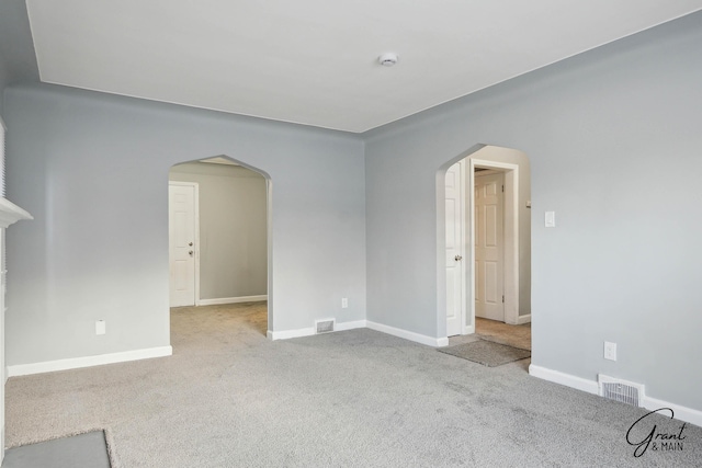 spare room featuring light colored carpet, arched walkways, visible vents, and baseboards