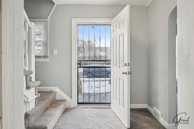 doorway to outside with carpet floors, arched walkways, visible vents, baseboards, and stairs