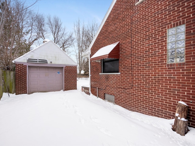 view of snowy exterior with an outbuilding, brick siding, and a detached garage