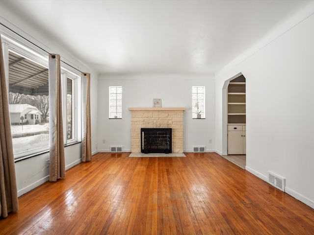 unfurnished living room featuring arched walkways, visible vents, and wood finished floors