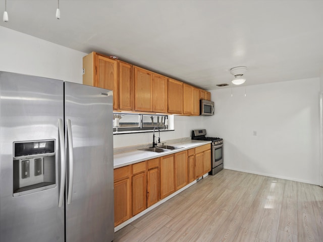 kitchen with brown cabinets, light countertops, appliances with stainless steel finishes, light wood-style floors, and a sink