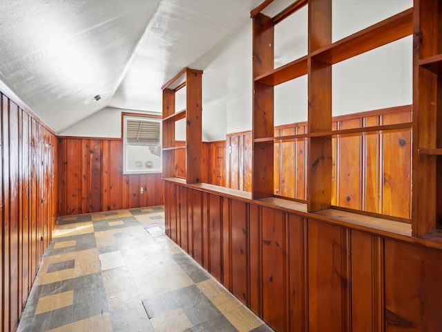 hallway featuring vaulted ceiling, light floors, and wood walls