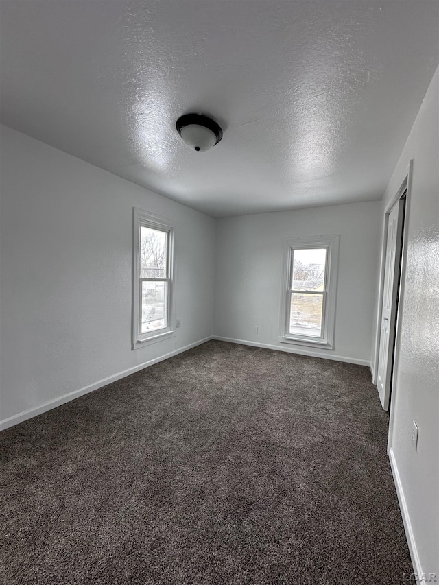 unfurnished room featuring baseboards, a textured ceiling, dark carpet, and a wealth of natural light