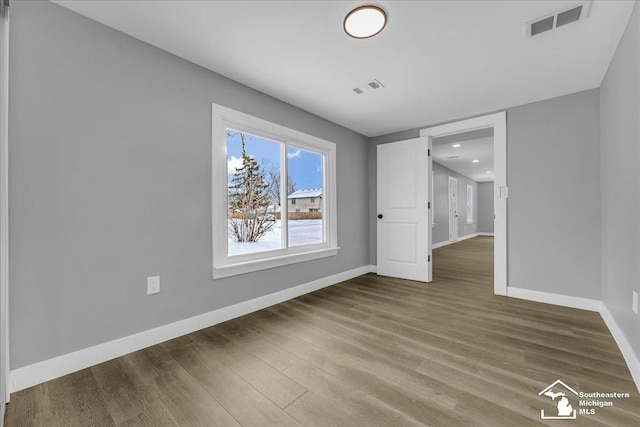 unfurnished room featuring wood finished floors, visible vents, and baseboards