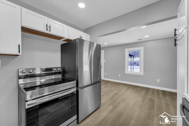 kitchen with a barn door, light wood-style flooring, stainless steel appliances, white cabinetry, and baseboards