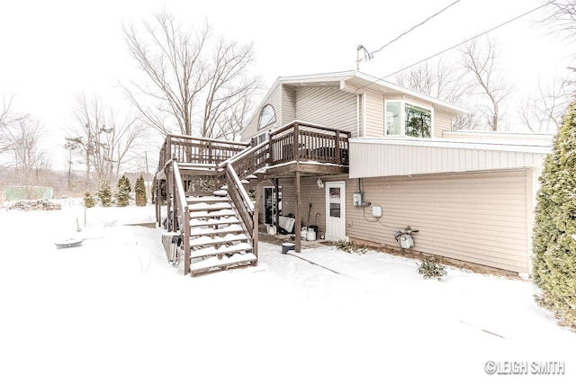 snow covered house with stairway and a wooden deck