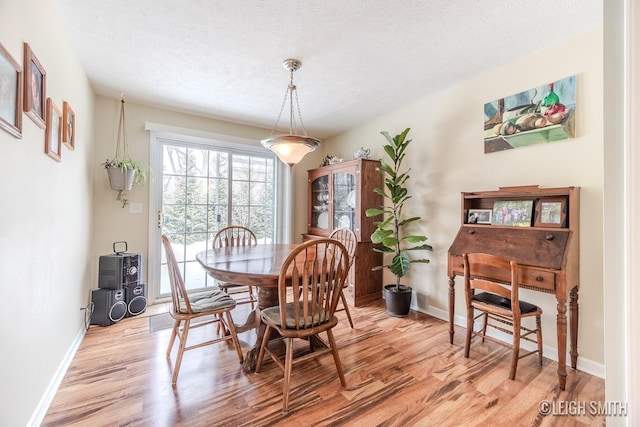 dining space featuring a textured ceiling, light wood-style flooring, and baseboards