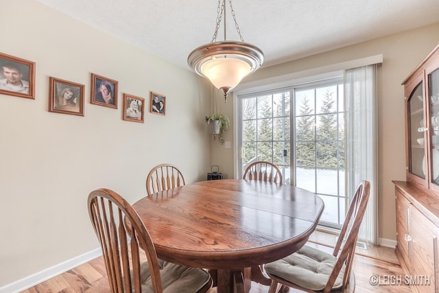 dining area with light wood-style floors, baseboards, and a textured ceiling