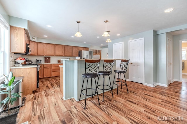 kitchen featuring appliances with stainless steel finishes, brown cabinets, light countertops, light wood-style floors, and pendant lighting