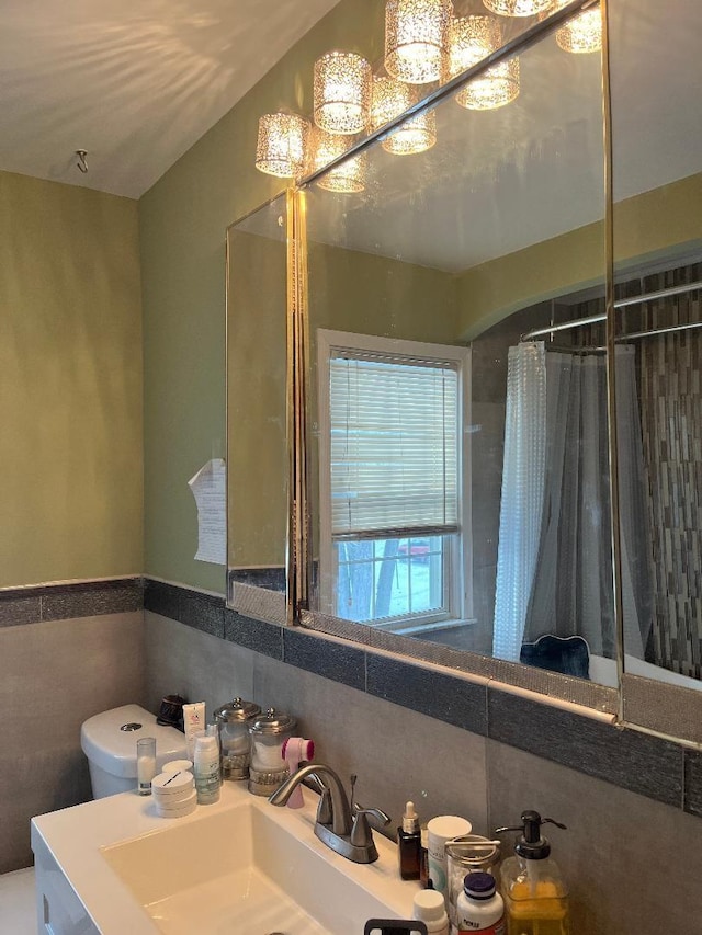 full bathroom featuring toilet, wainscoting, a sink, and tile walls