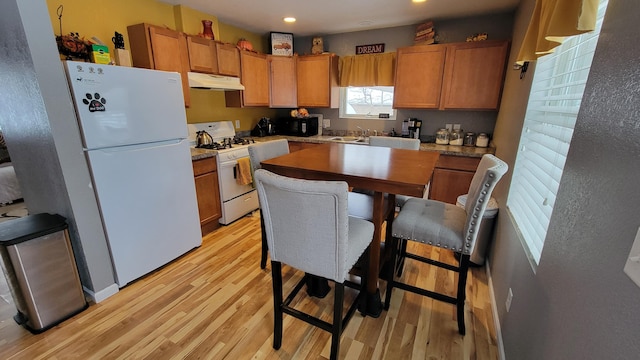 kitchen featuring light wood-type flooring, white appliances, brown cabinets, and under cabinet range hood