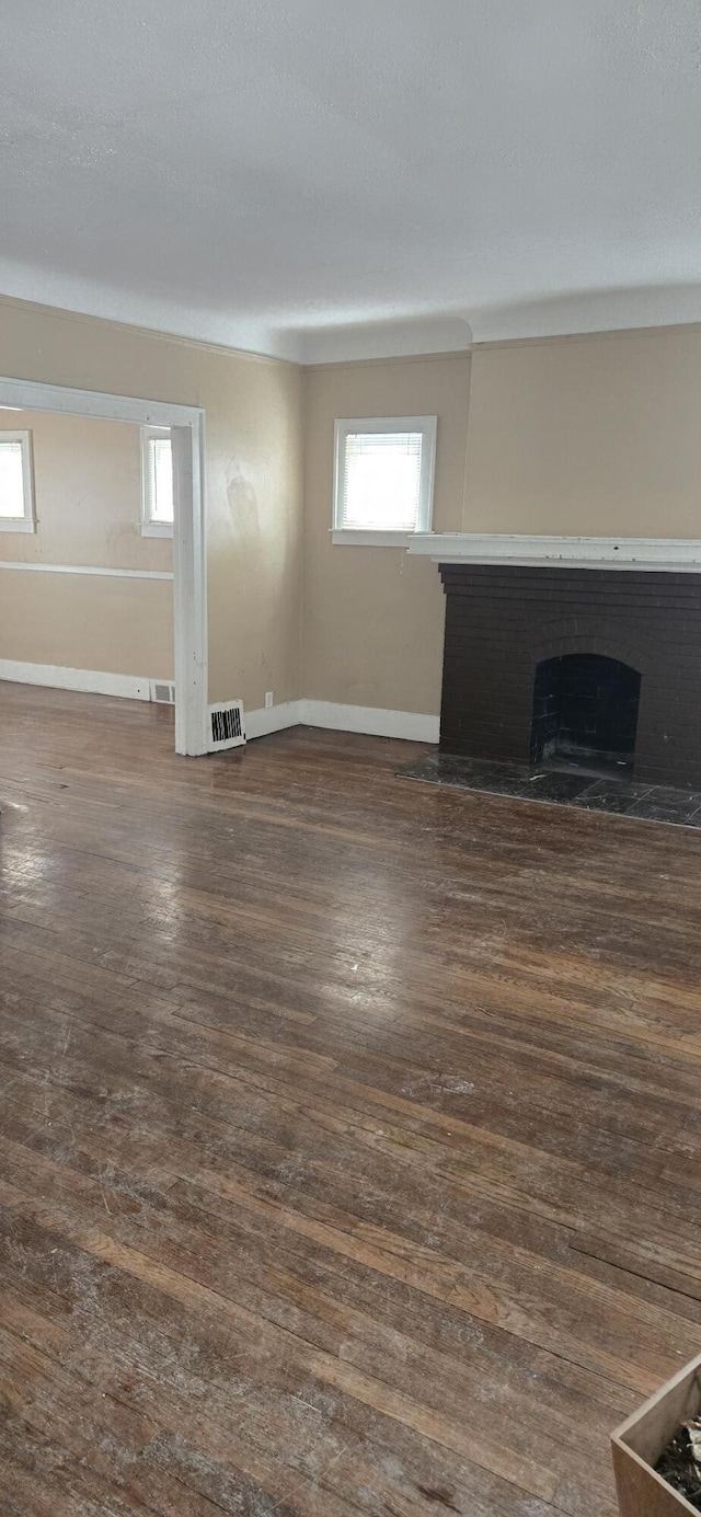 unfurnished living room with baseboards, a fireplace, visible vents, and dark wood-type flooring