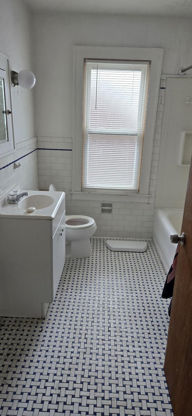 full bathroom featuring toilet, bathing tub / shower combination, vanity, tile walls, and wainscoting