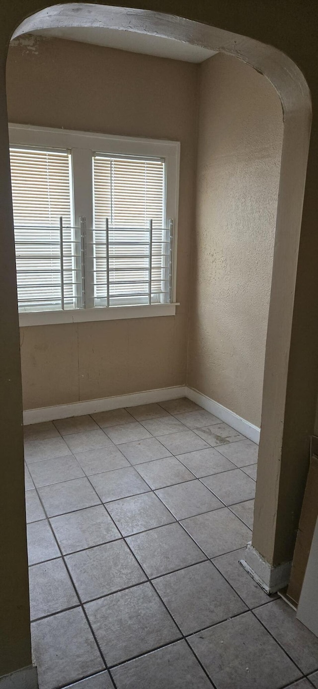 empty room featuring light tile patterned floors, arched walkways, and a wealth of natural light