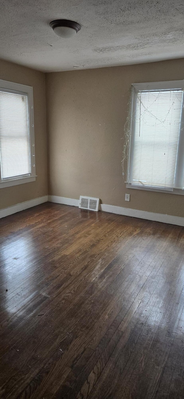 empty room with dark wood-style floors, a wealth of natural light, and visible vents