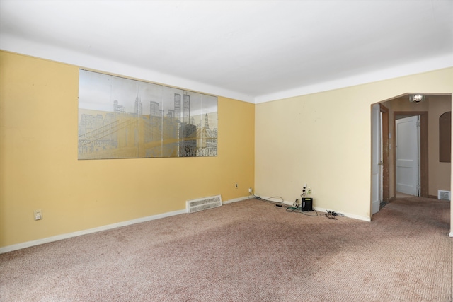 carpeted spare room with baseboards, visible vents, and arched walkways