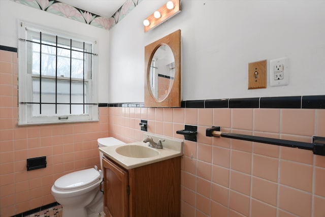 half bath featuring tile walls, a wainscoted wall, vanity, and toilet