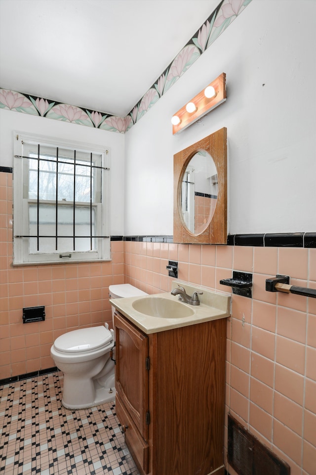 half bath featuring toilet, a wainscoted wall, tile walls, and vanity