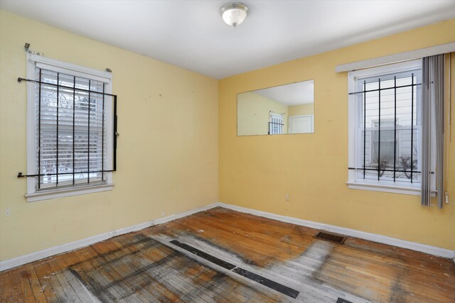 unfurnished room featuring plenty of natural light, wood finished floors, visible vents, and baseboards