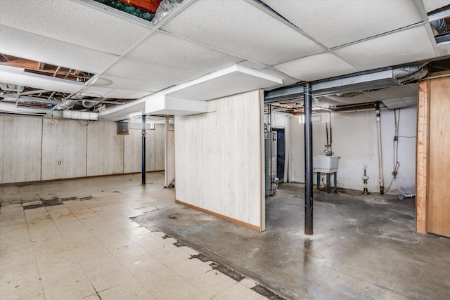 unfinished basement featuring gas water heater, a sink, a paneled ceiling, and tile patterned floors