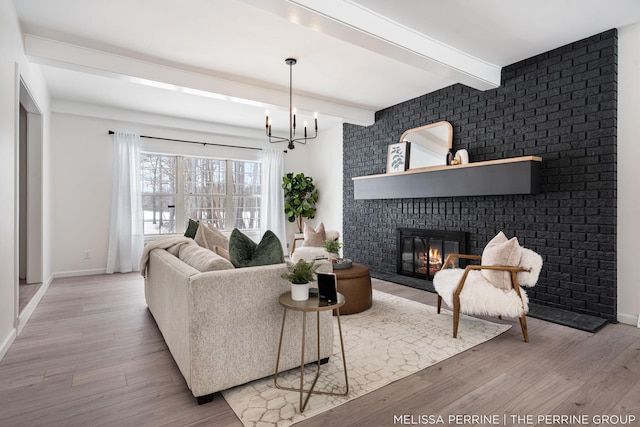 living room featuring a brick fireplace, baseboards, beamed ceiling, light wood-style floors, and a chandelier