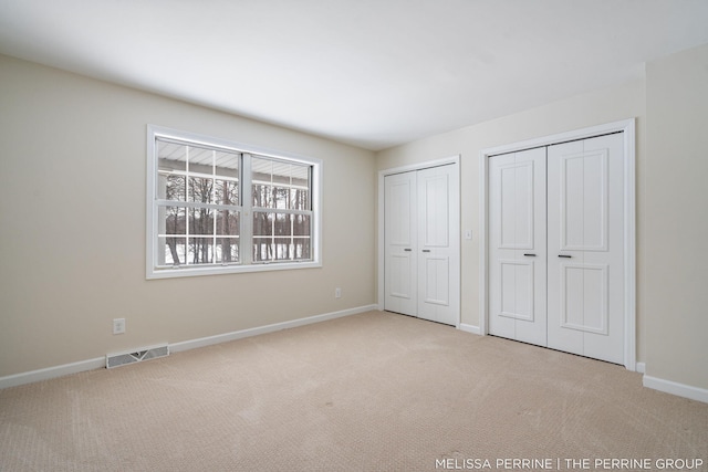 unfurnished bedroom featuring light carpet, baseboards, visible vents, and multiple closets