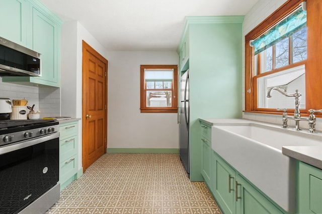 kitchen featuring tasteful backsplash, light countertops, appliances with stainless steel finishes, a sink, and baseboards