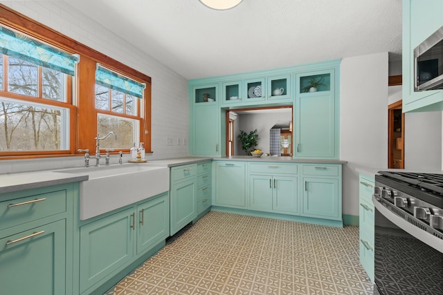 kitchen with glass insert cabinets, stainless steel appliances, light countertops, light floors, and a sink