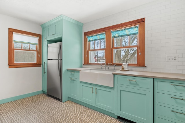 kitchen featuring a sink, baseboards, light countertops, freestanding refrigerator, and light floors