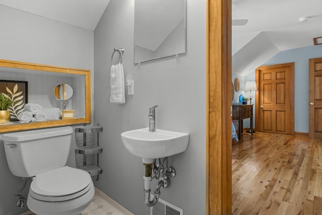 bathroom with lofted ceiling, toilet, a textured ceiling, wood finished floors, and baseboards