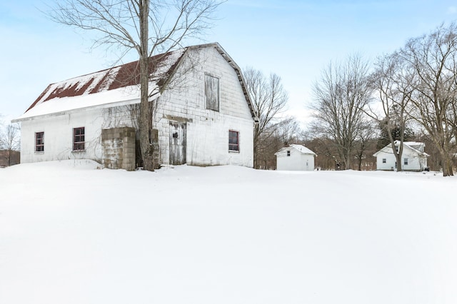 view of snow covered exterior featuring an outdoor structure, a barn, and a gambrel roof