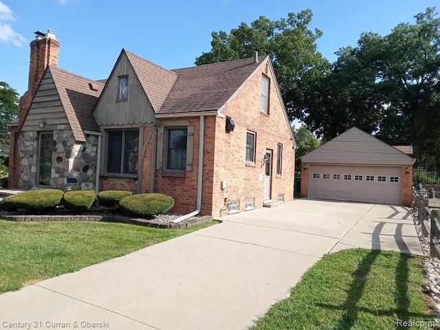 tudor home with a garage, a chimney, roof with shingles, a front lawn, and brick siding